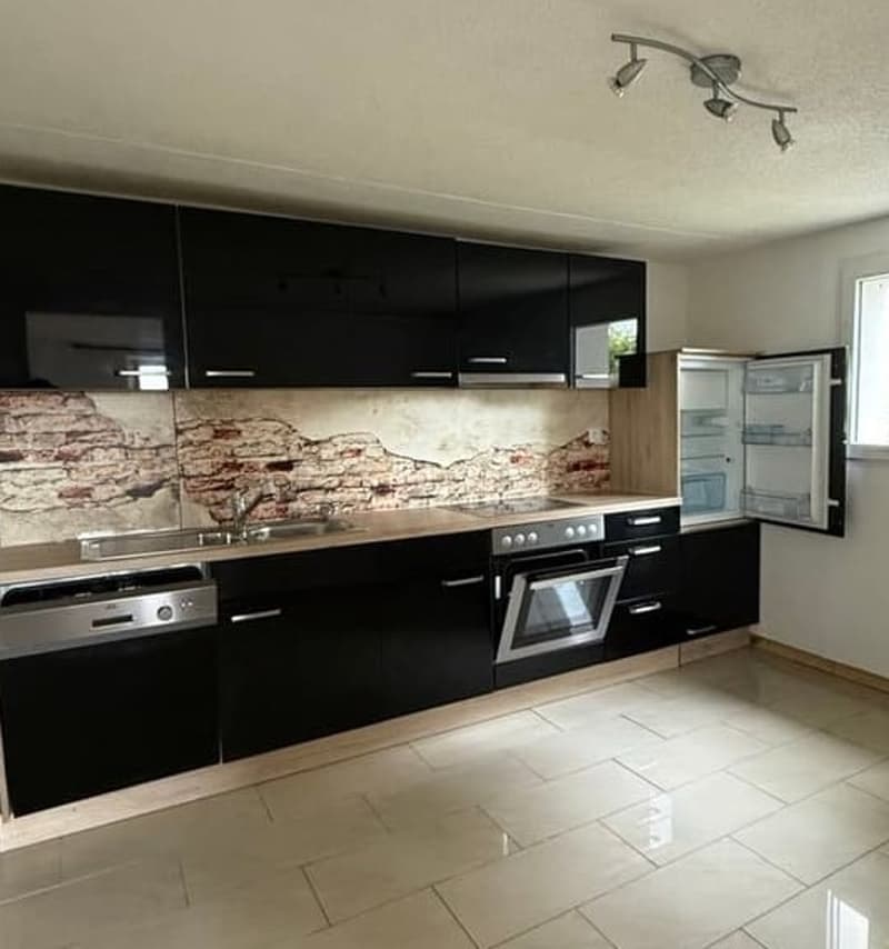 Modern kitchen with black cabinets, stainless steel appliances, and a brick backsplash. The kitchen has a dishwasher and appears to be a spacious and well-designed space.