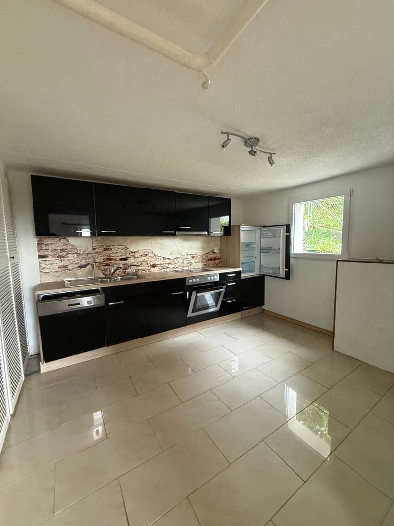 Modern kitchen with black cabinets, stone backsplash, stainless steel appliances including a dishwasher, and tiled flooring.