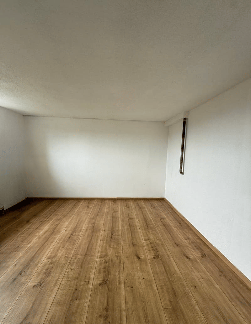 Empty room with white walls and hardwood flooring. The room appears to be a living room or bedroom with no visible furniture or decor.