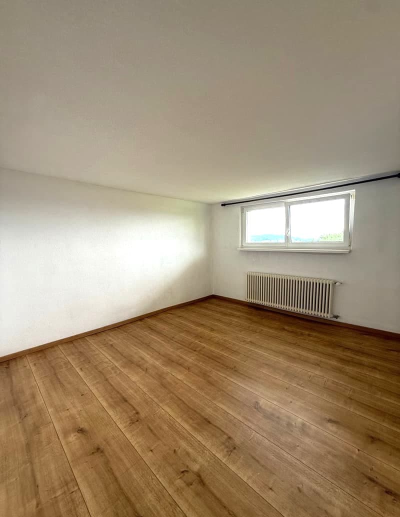 Empty room with white walls, hardwood flooring, and a window providing natural light.