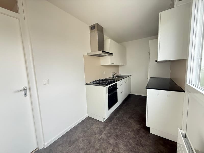 modern kitchen with white cabinets, black countertops, gas stove, oven, sink, and a window