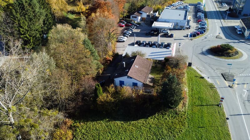 Two buildings, multiple cars parked, one building is a gas station, another has a garage.