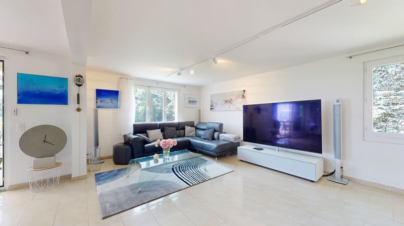 living room with black leather sofa, glass coffee table, TV on a white stand, large windows, artwork on the wall