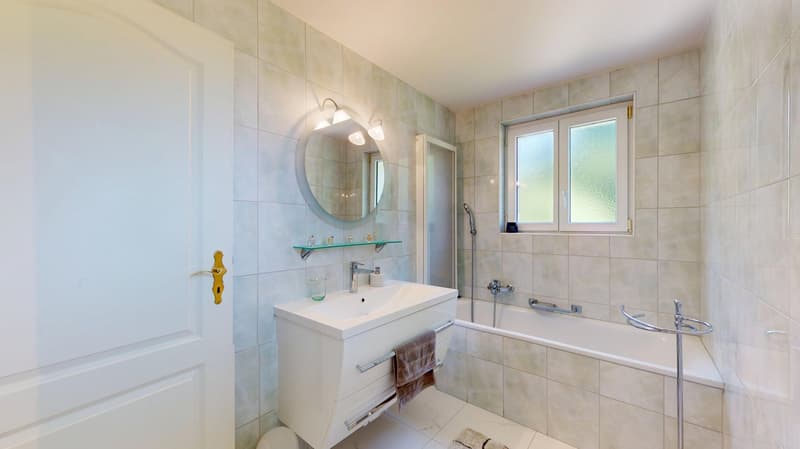 Bathroom with tub, white sink, round mirror, shelf, and a window
