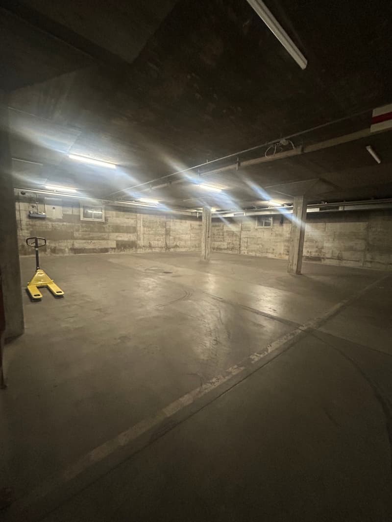 underground parking lot, cement floor, fluorescent ceiling lights, empty, pillars, windows on wall