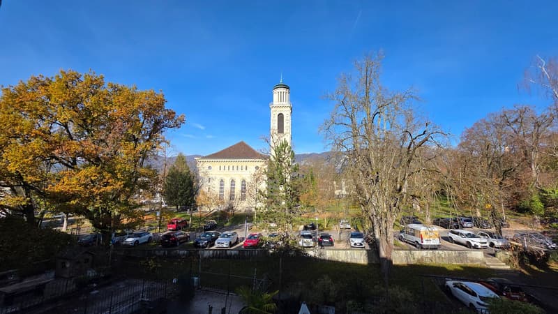 Church with a tower, church in the center, surrounded by trees and parked cars, buildings in the background