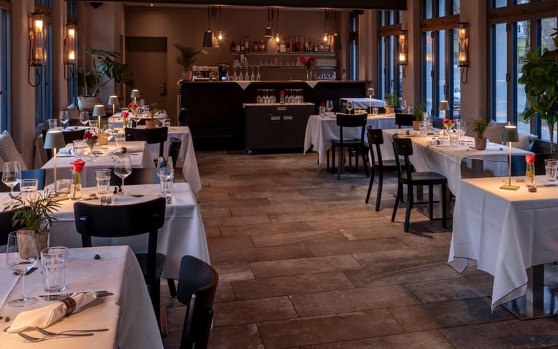 restaurant interior, wooden floors, white tablecloths, chandelier lamps, flowers, chairs, round tables, large windows