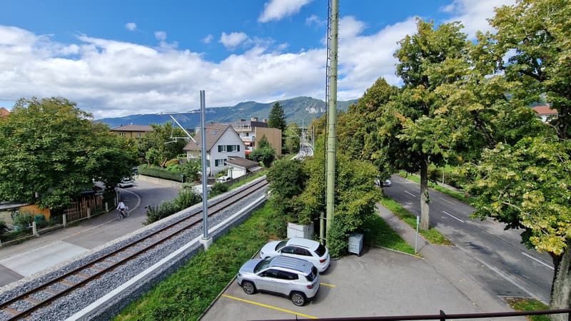 3 cars parked in lot, train tracks, electric poles, road, buildings, trees, mountains