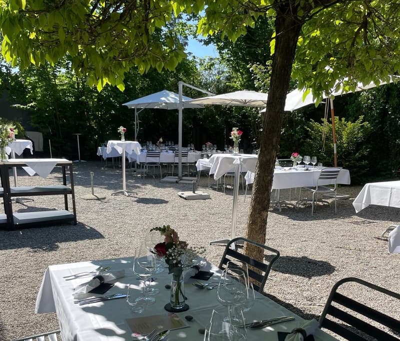 garden area, multiple tables and chairs set up under umbrellas, floral arrangements on the tables, stone floor