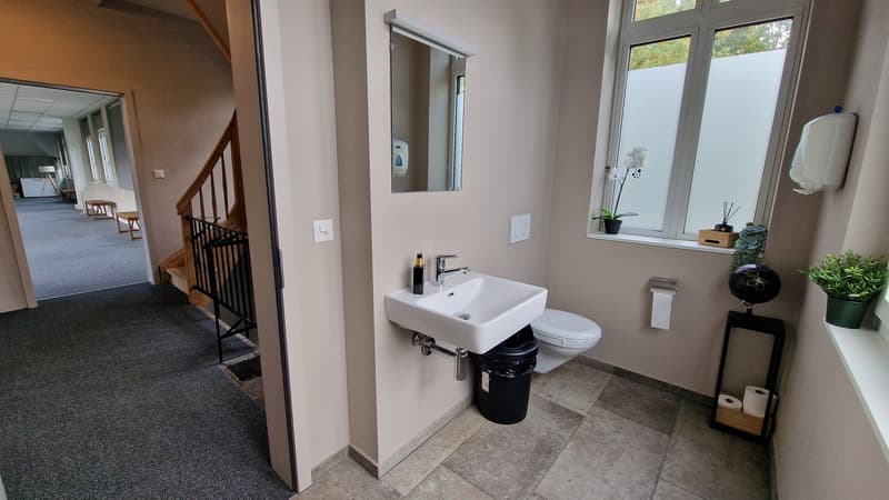 clean white sink, black trash can, toilet, mirror, tiled floor, open door to hallway
