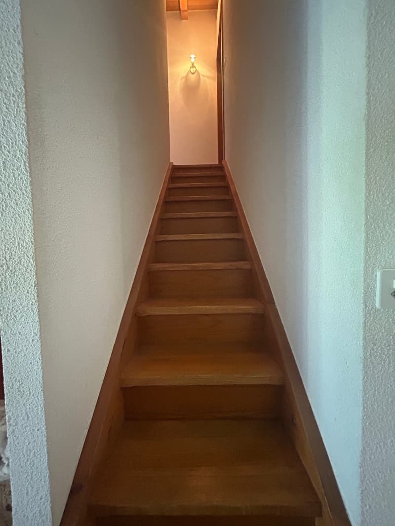 Wooden staircase with light on the wall and white walls.