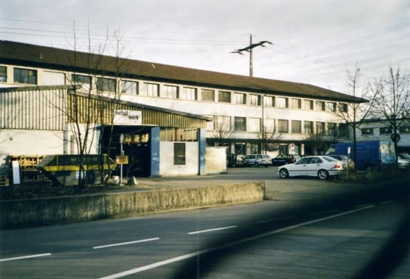 A building with several windows, parked cars in front, street light pole, road.