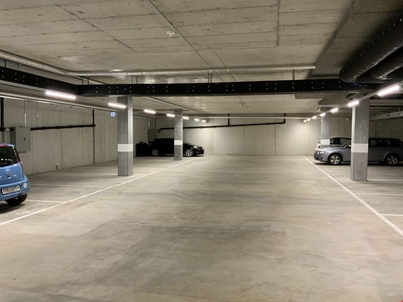 large underground parking lot with 3 vehicles parked, several empty parking spaces, modern ceiling design