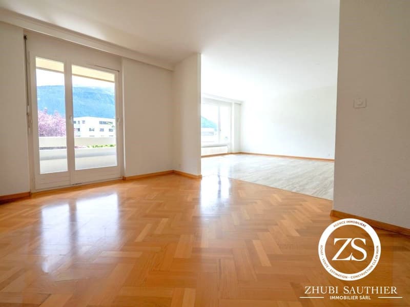 Spacious room with hardwood floors, sliding glass doors to balcony, large windows with views, white walls