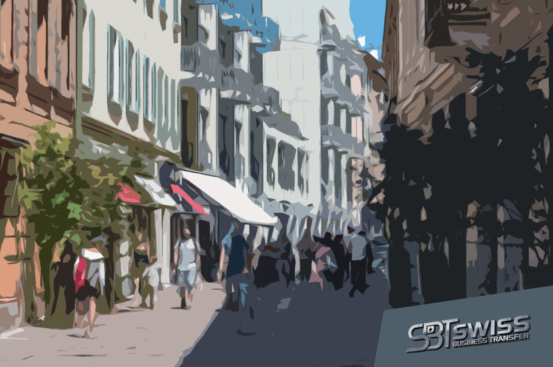Busy urban street with shops, pedestrians, tall buildings, trees, awnings, and shadows