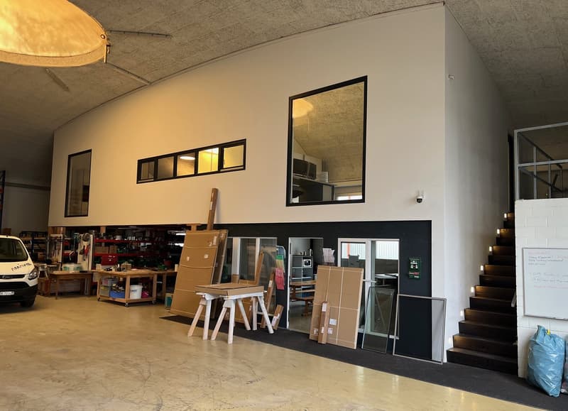 warehouse interior with white walls, a white ceiling, several windows, a security camera, stairs on the right, tables, shelves, cardboard boxes, a car parked on the left