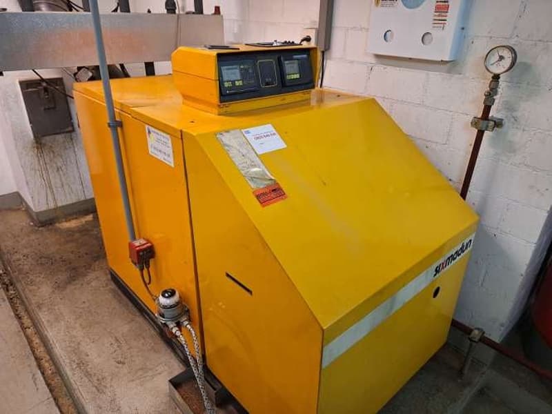 Yellow machine with digital display, white label with red sticker, pipes, pressure gauge attached to the wall