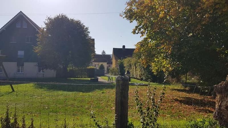 House with fenced yard, visible from the street, green trees, house in the background