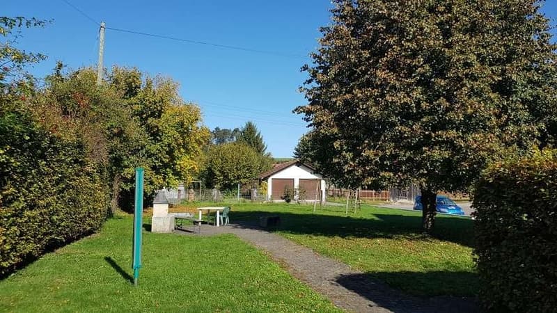 large open green area with small path leading to house, blue car parked