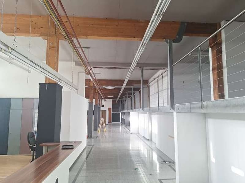 open space with wooden ceiling, raised ground floor, metal balustrade, tiled floor, empty chairs, standing ladder, office walls, windows