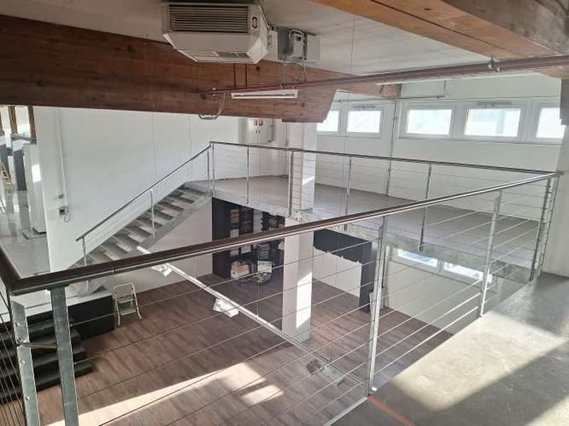 Open space with two levels, stairs, metal railings, ceiling fan, wooden ceiling beams, white walls, floor made of dark wood