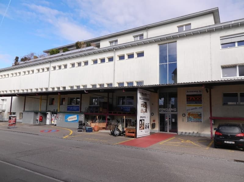 Modern white building with large windows, entrance, parked car, and red carpet