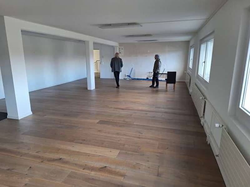 Large empty room with hardwood floors, large windows, and white walls