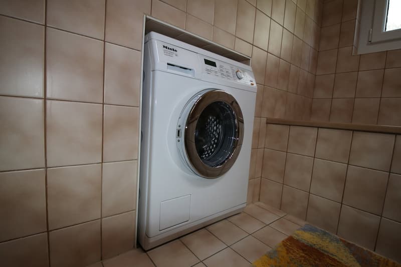 Built-in white washing machine, tiled walls, small rug, window