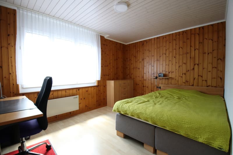 bedroom with bed, desk, chair, wooden walls, window, heater