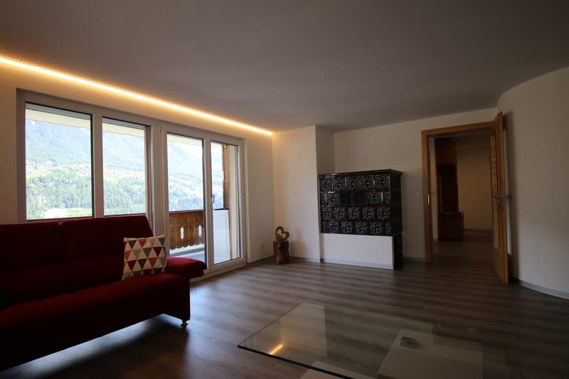 large couch, coffee table, sliding glass doors, floor to ceiling windows, wooden floor, mountains in background
