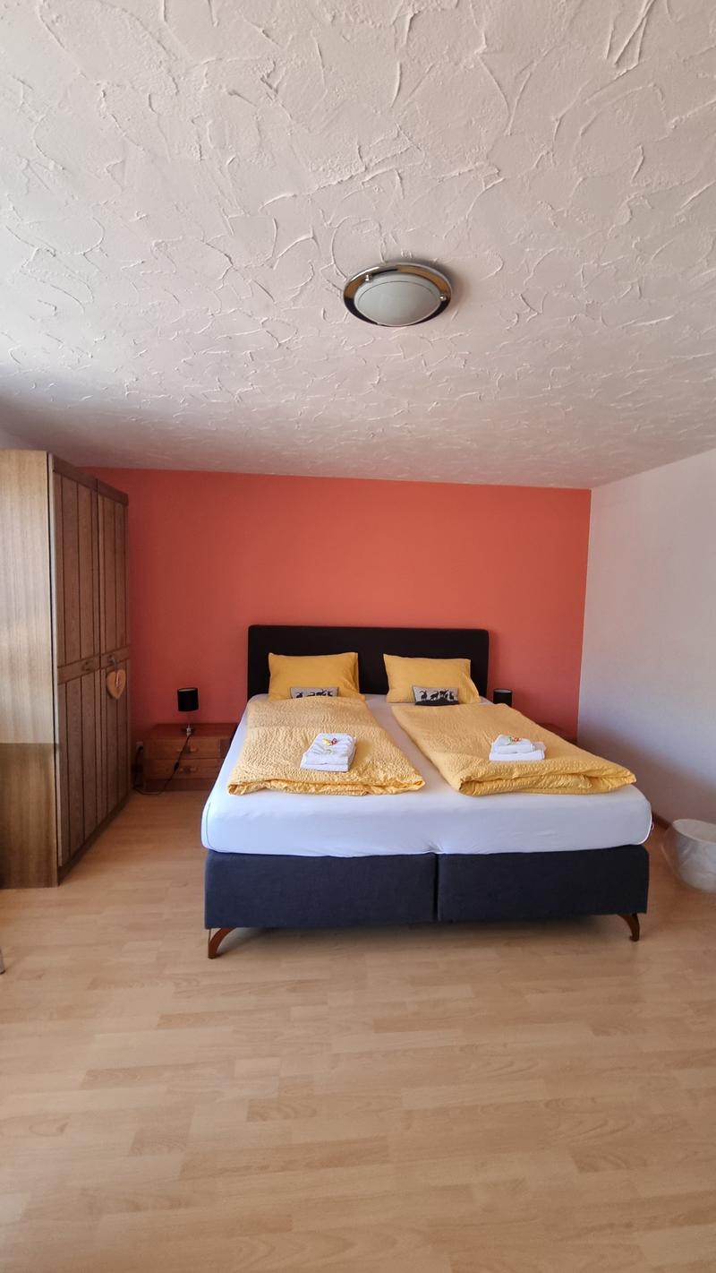 double bed with yellow covers, white nightstands with lamps, wardrobe, wooden floor, orange wall, white ceiling