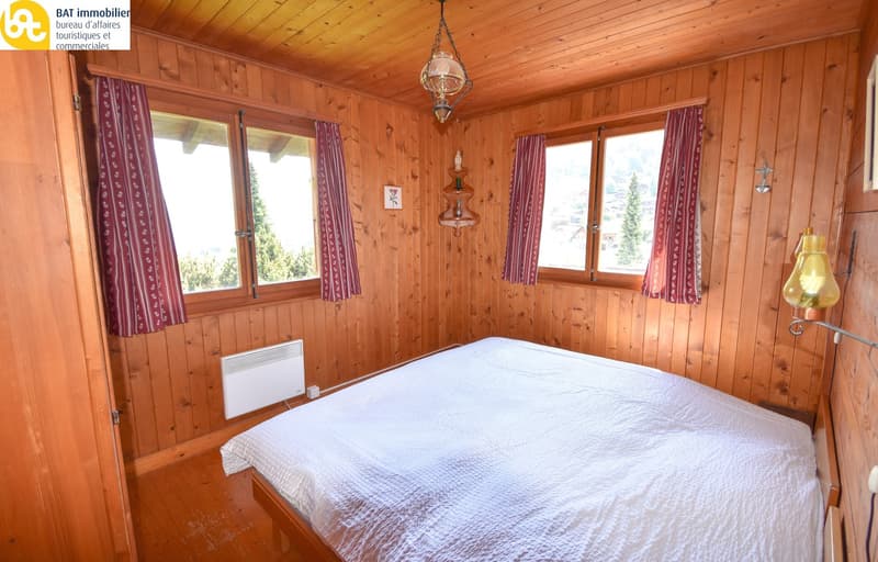 Single bed, wooden wall, radiator, 2 windows with curtains, wooden floor, lamp, window view of mountain