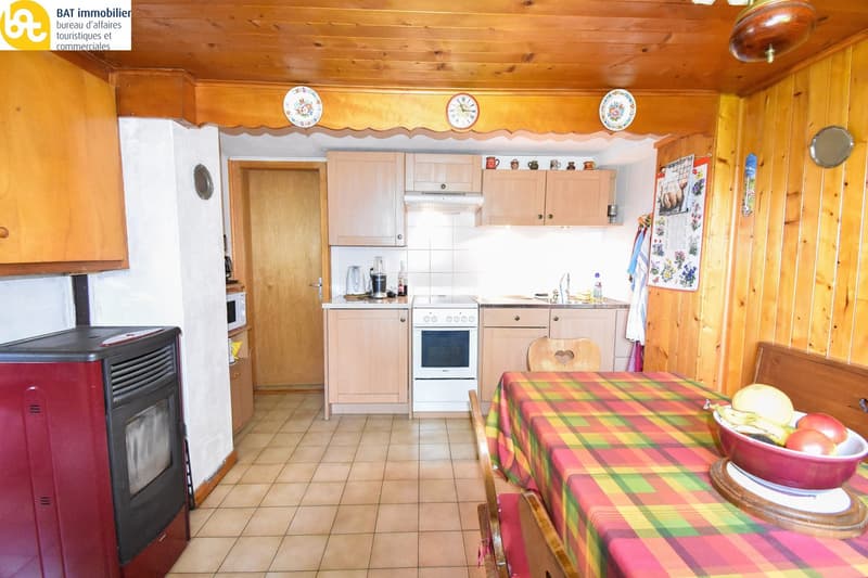 wooden cabinets, white stove, tiled floor, wooden dining table with fruit bowl, wall clocks, wall hooks