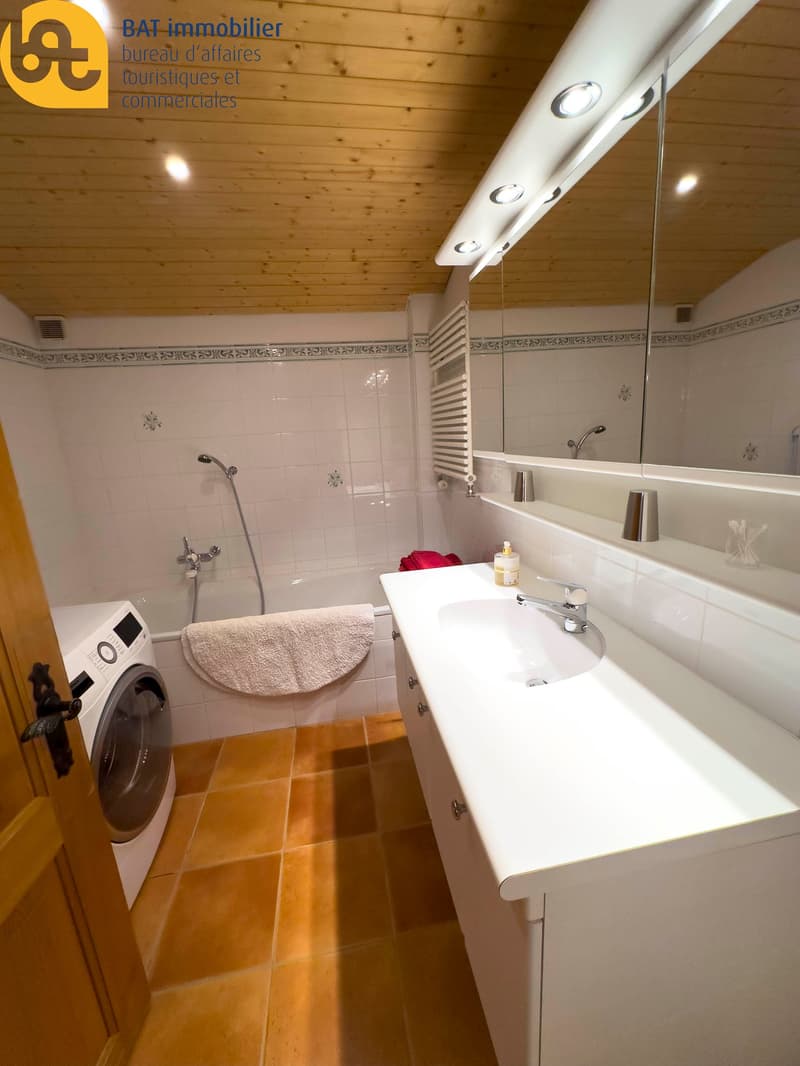 Bathroom with wooden ceiling, tiled walls, vanity sink, mirror, and a washing machine.