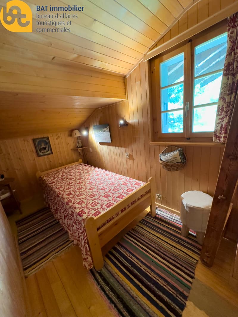 Cozy wooden bedroom with a patterned bedspread, wooden walls and ceiling, and a fireplace visible.