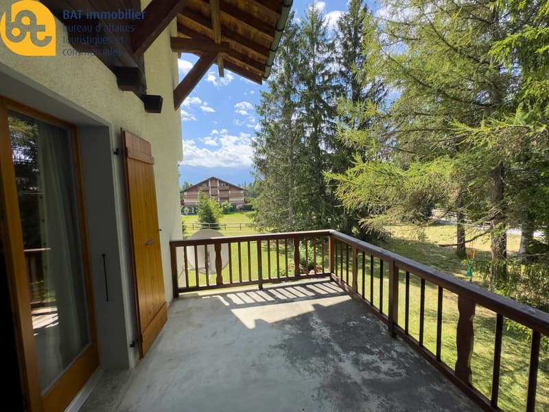 Balcony with wooden railing, overlooking a grassy area with trees