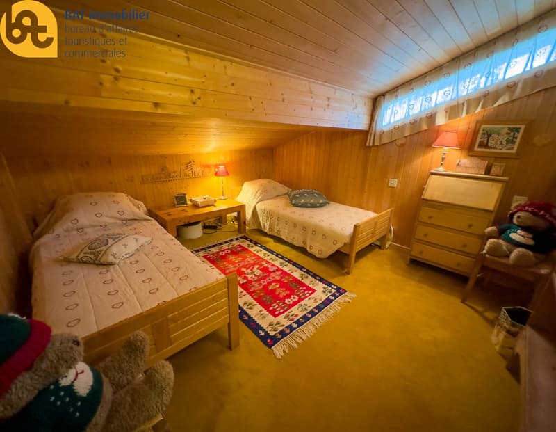 Cozy wooden bedroom with two twin beds, wooden furniture, and a colorful patterned rug on the floor.