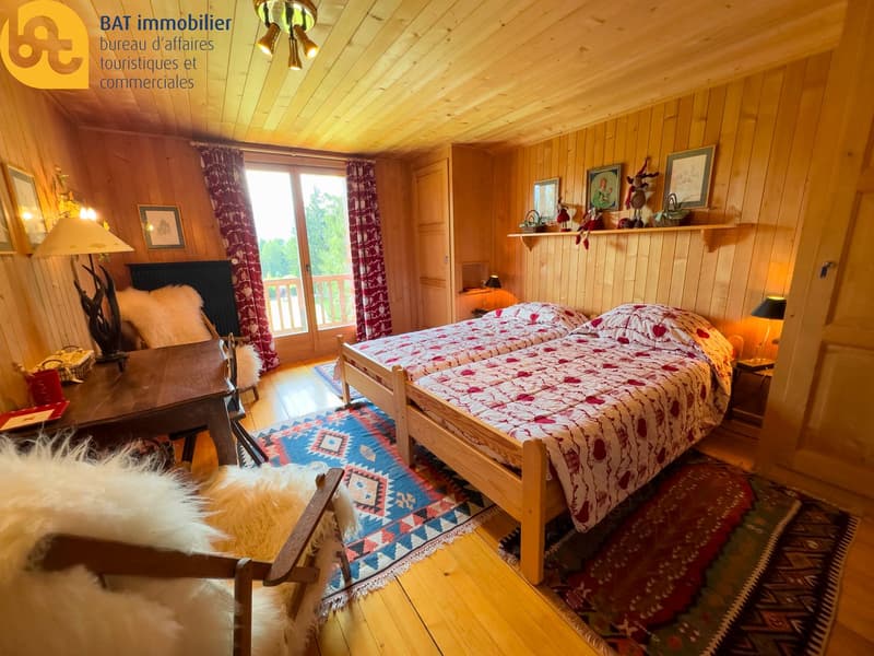 Cozy wooden bedroom with large windows, patterned bedding, wooden furniture, and decorative accents.
