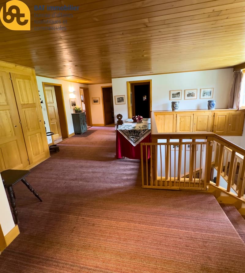 Spacious living room with wooden paneled walls and ceiling, hardwood floors, a fireplace, and various decorative items such as framed artwork and vases on a wooden cabinet.
