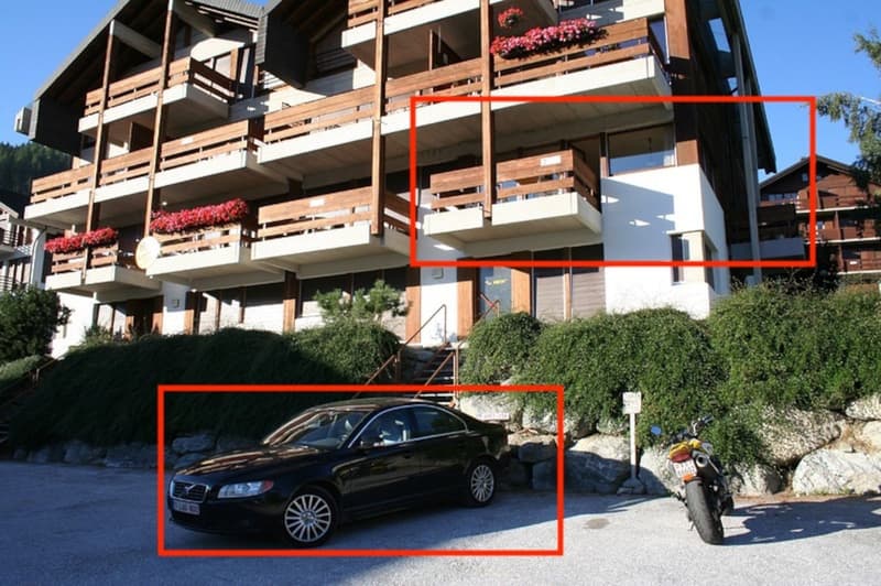 Multi-story apartment building with wooden balconies, parking spaces in front of the building