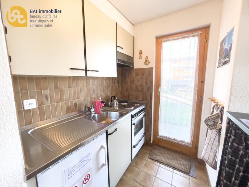 Compact kitchen with white cabinets, tiled backsplash, stainless steel sink and appliances, including a dishwasher, and a window providing natural light.