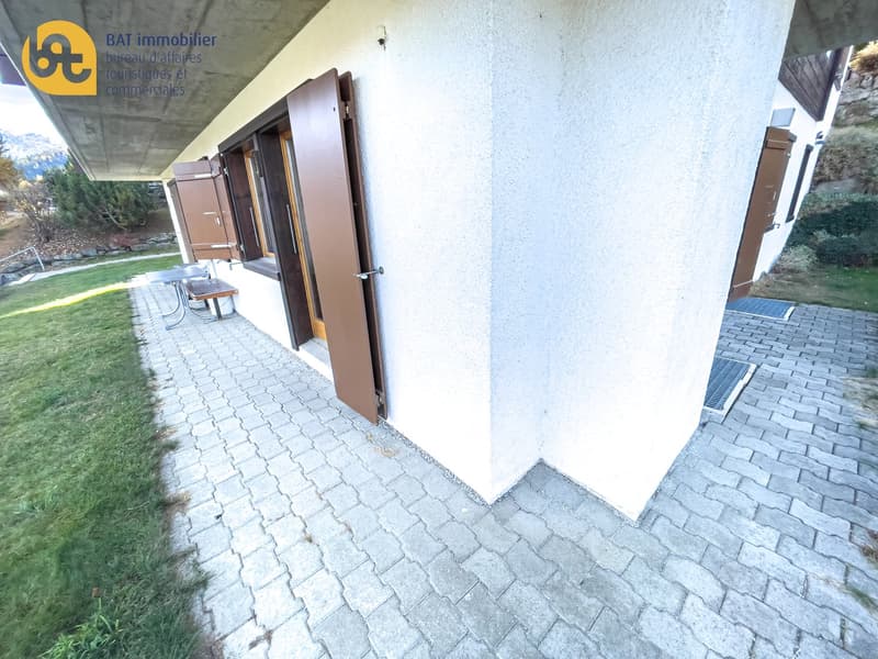 Exterior view of a commercial property with a paved walkway, stone walls, and a sign for a real estate agency called 'BAT immobilier'
