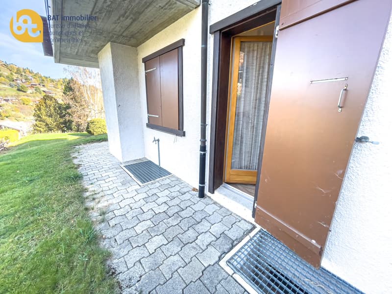 Exterior of a commercial property with a paved walkway, a metal door, and a window. The property has the logo of a real estate agency, BAT Immobilier, displayed on the facade.