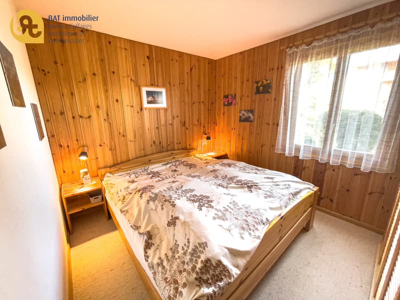Cozy bedroom with wooden walls, large bed with patterned bedding, nightstand, and curtains
