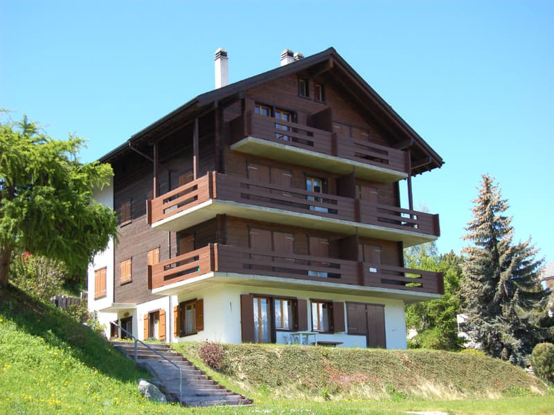 3-story wooden chalet-style house with balconies, located on a hillside surrounded by trees and greenery