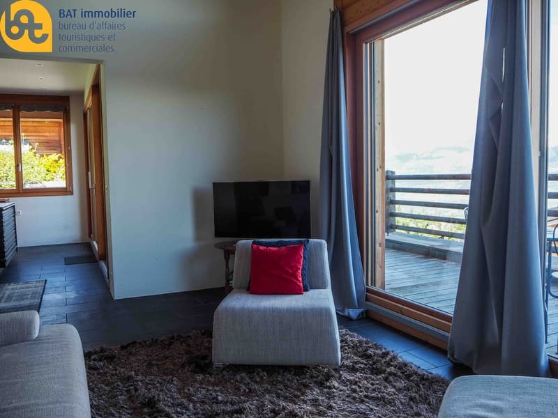 Living room with large windows, gray sofa, red accent pillow, TV, and access to a balcony or terrace with a view.