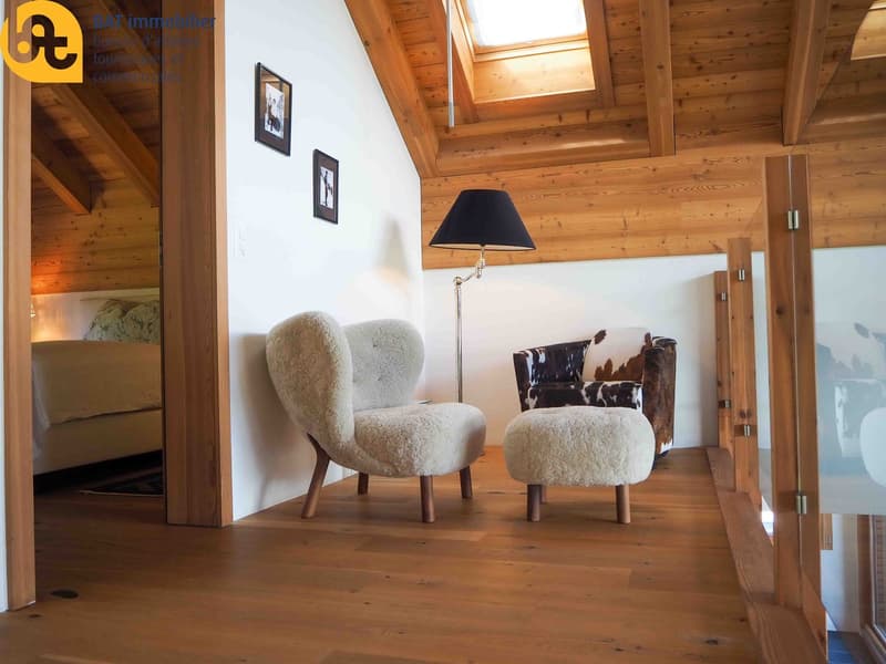 Cozy living room with wooden ceiling and walls, two plush armchairs, a floor lamp, and framed artwork on the walls.
