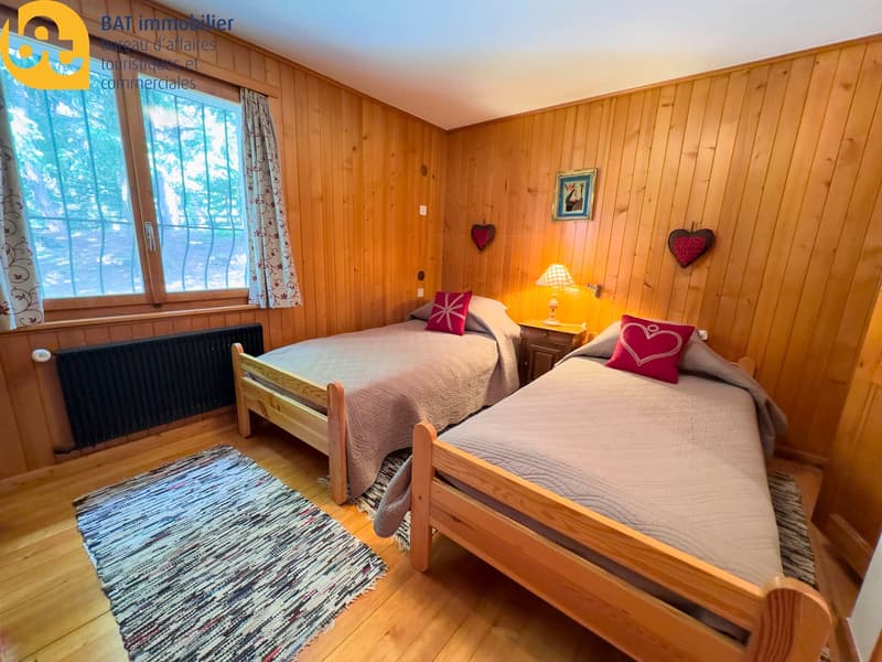 Cozy bedroom with wooden walls and floors, two twin beds with red and pink accents, a rug, and a fireplace