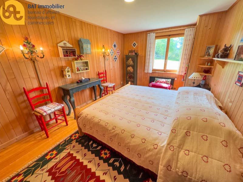 Cozy wooden bedroom with a large bed, patterned bedding, wooden furniture, shelves with decorative items, and a fireplace