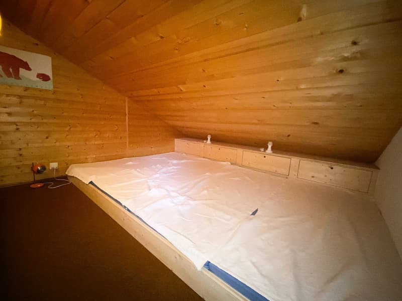 small room with a single bed, wooden paneling on the wall, wooden flooring, lamp